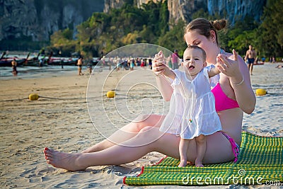 Little baby hold mother`s hands and trying to walk on a beach. Happy screaming toddler Stock Photo