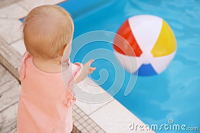 Little baby reaching for inflatable ball at swimming pool. Dangerous situation Stock Photo