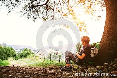 Little backpacker traveler rest under tree on country road Stock Photo