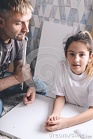 Little beautiful caucasian girl and her loving father are assembling furniture together. Housework. Family indoor activity. Front Stock Photo