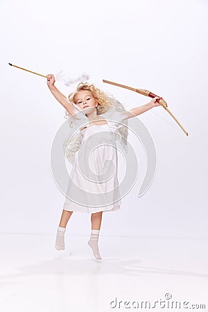 Little beautiful girl, child in image of cupid, angel holding bow isolated over white studio background. Valentines Stock Photo