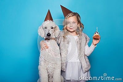 Little beautiful girl with dog celebrate birthday. Friendship. Love. Cake with candle. Studio portrait over blue background Stock Photo