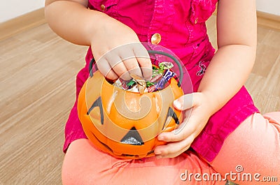 Little beautiful girl sitting with a pumpkin with candies in her hands, on Halloween. Stock Photo