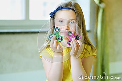 Little beautiful girl in yellow t-shirt is playing with two spinners in hands Stock Photo