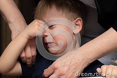 A little blond boy, age 3, is crying and his mother calms him down. female hands close-up on a black background Stock Photo