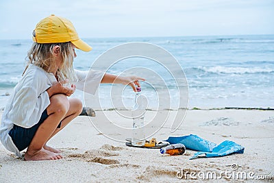 Little boy picks up glass bottle from garbage lying on an ocean shore Stock Photo