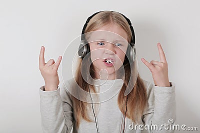 Blond girl with headphones listening music and singing. Cute little girl making a rock-n-roll sign. Stock Photo