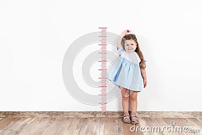 Little blond girl measuring height on white wall. Stock Photo