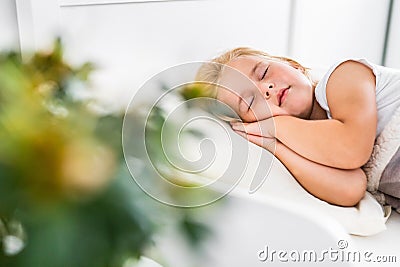 Little blond girl sleeping on white bed with her hands under her cheek. Carefree, childhood. Stock Photo