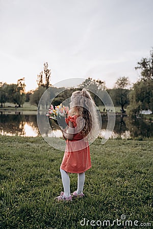 A little blonde with a bouquet in her hand looks into the distance with her back to the camera Stock Photo