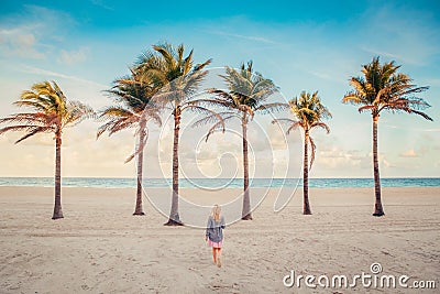 Little blonde Caucasian girl walking on empty Hollywood ocean beach in Florida. Child among tall palm trees on summer sunny day at Stock Photo