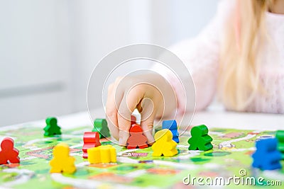 little blonde girl hold red people figure in hand. yellow, blue, green wood chips in children play - Board game and kids leisure c Stock Photo