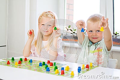 little blonde girl hold red people figure in hand. yellow, blue, green wood chips in children play - Board game and kids leisure c Stock Photo