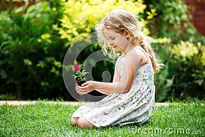 Little blonde girl holding young flower plant in hands on green background. Stock Photo