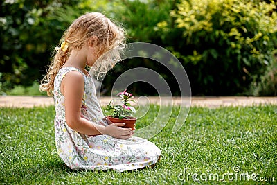 Little blonde girl holding young flower plant in hands on green background. Stock Photo