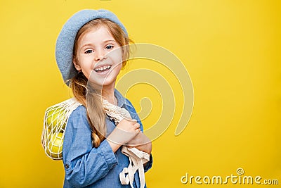 A little blonde girl with long hair in a blue dress and beret on a yellow isolated background. Child with apples. Stock Photo