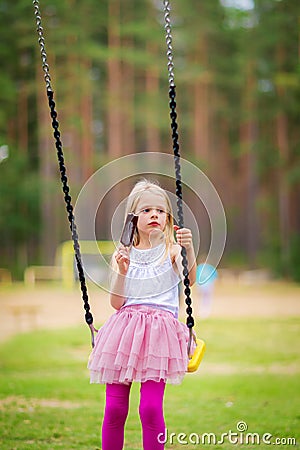 Little blonde girl smiling swinging outdoors on a playgroung Stock Photo