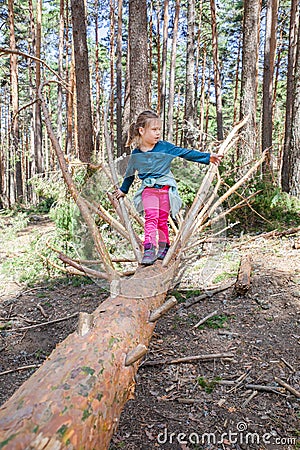 Little blonde girl standing on tree trunk Stock Photo