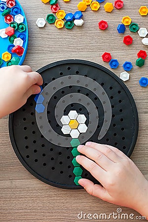 Little blonde girl in a white tshirt playing with plastic multicolor mosaic at home or preschool. Early education Stock Photo