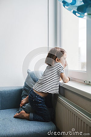 Little bored girl sitting on the couch at home and looking at the window Stock Photo
