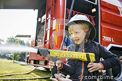 Little fireman holding firehose nozzle and splashing water Stock Photo