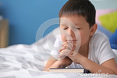 Little boy with Bible praying in bedroom Stock Photo