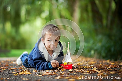 Little boy with boat, lying on the ground in a park Stock Photo