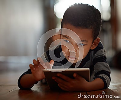 Little boy, browsing and on digital tablet or playing games or streaming video on the internet and lying on the floor at Stock Photo