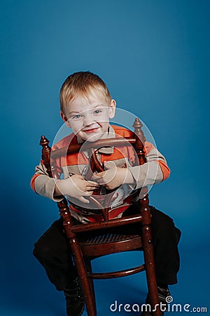 A little boy in a cap sits on a chair and smiles Stock Photo