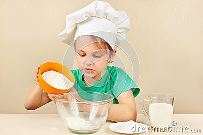 Little boy in chef hat pours flour for baking cake Stock Photo