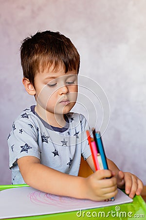 Little boy drawing with color pencils. There are many colored pencils in the boy`s hands. Small boy draws at the table Stock Photo