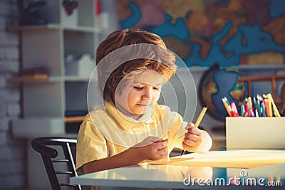 Little boy drawing, education and daycare. Portrait of cute boy with sketch pen and paper at desk in classroom. Stock Photo