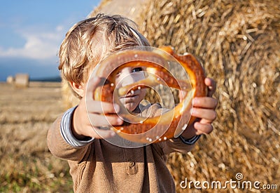 Little boy eating German pretzel on goden hay field Stock Photo
