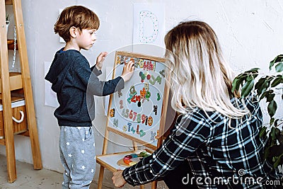 Little boy and educator playing and studying numbers, letters and alphabet on magnetic board in playroom backview Stock Photo