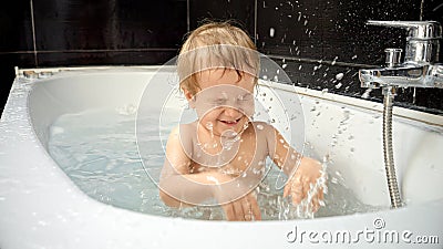 A little boy giggles and splashes in his bath, creating a spray of water. Pure happiness and carefree nature of childhood Stock Photo