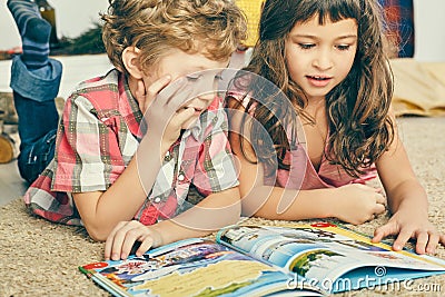 Little Caucasian curly boy and girl lying on the floor and reading an illustrated book. Stock Photo