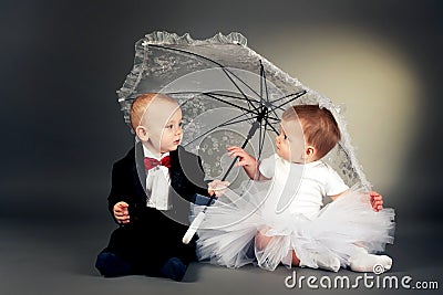 Little boy and girl sitting under umbrella Stock Photo