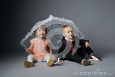 Little boy and girl sitting under umbrella Stock Photo