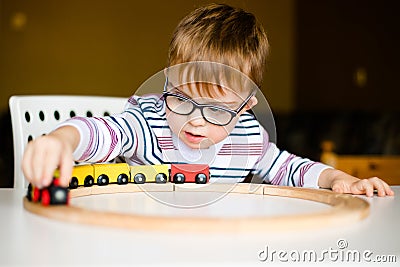 Little boy in the glasses with syndrome dawn playing with wooden railways Stock Photo