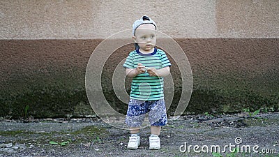 Little boy in green T-shirt and hat alone near plastered wall Stock Photo