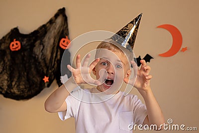 A little boy in a Halloween cap makes a scary frightening face on Halloween. Hands raised, halloween themed background Stock Photo