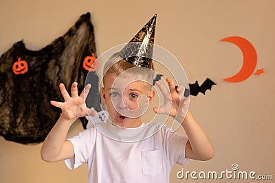 A little boy in a Halloween cap makes a scary frightening face on Halloween. Hands raised, halloween themed background Stock Photo