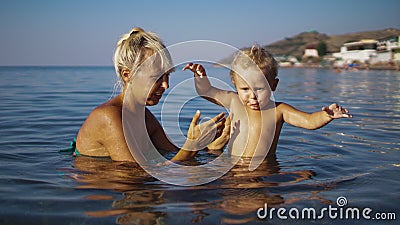 Little boy and his blond mom goes into water to swim and playing in the sea Stock Photo