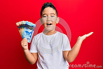 Little boy hispanic kid holding canadian dollars celebrating achievement with happy smile and winner expression with raised hand Stock Photo