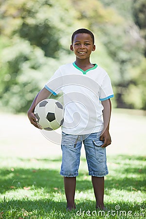 Little boy holding football in the park smiling at camera Stock Photo