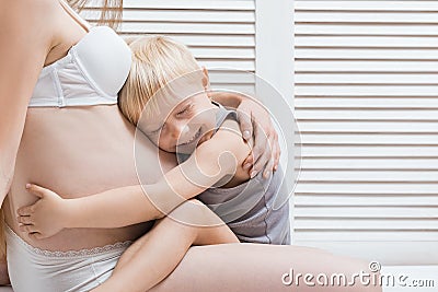 Little boy hugging his stomach of pregnant mother and laughs. young pregnant woman and the eldest son Stock Photo