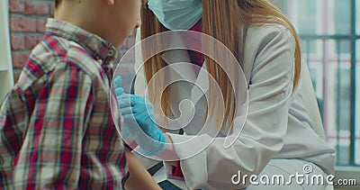 Little boy kid in protective medical mask is getting vaccinated. Female doctor injects vaccine into child& x27;s shoulder. Stock Photo