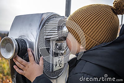 Little boy in a knitted hat looks through the observation coin binoculars at the autumn maple grove on the mountains in Vermont Stock Photo