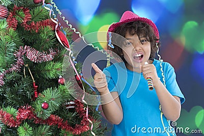 Little boy laughing on new year`s eve, wearing shiny hat and blowing horn, Stock Photo