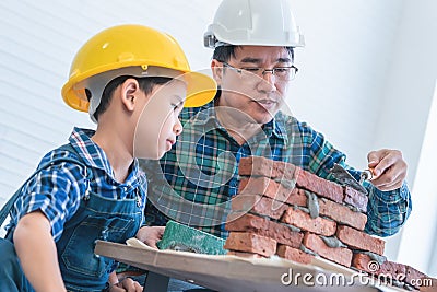 Little boy learning how to build brick wall from his construction father Stock Photo
